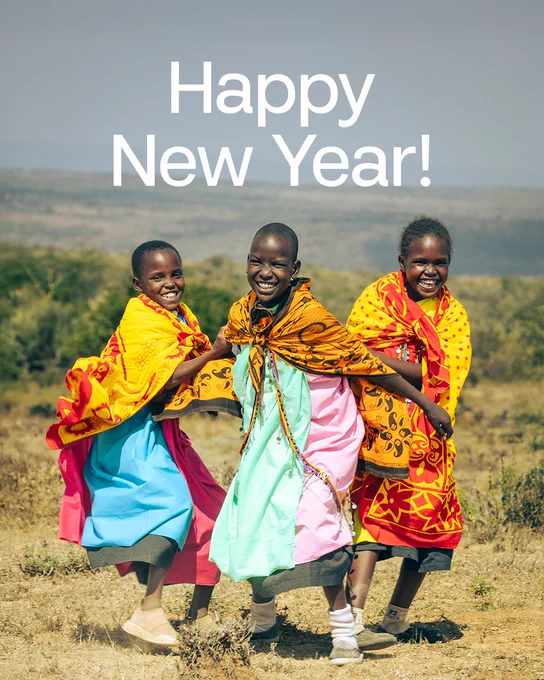 Three individuals in colorful traditional attire smiling and walking joyfully in a field with a 'Happy New Year!' greeting above them.