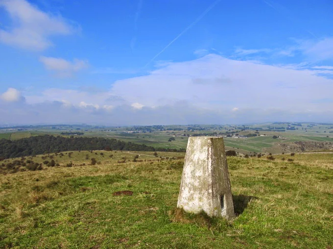Landscape view from atop a hill looking down. There is a stone in the ground, and blue skies in the background.