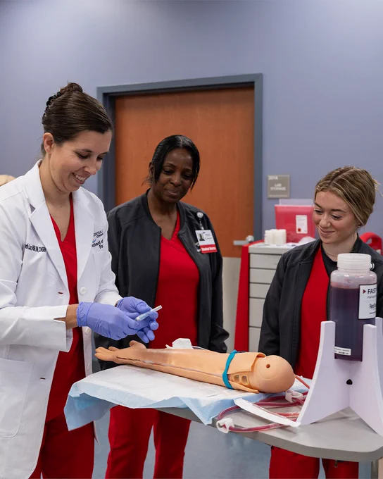 Two medical students and their teacher set an iv on a fake arm
