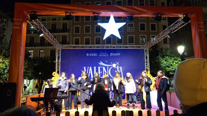 Coro de personas cantando en un escenario al aire libre en Valencia, bajo una estrella iluminada. Un teclado está a la izquierda.