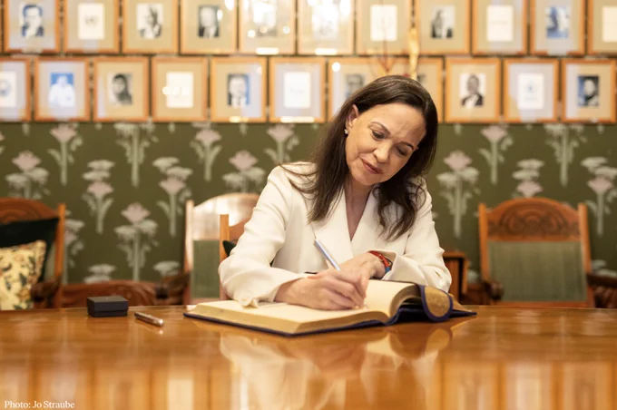 A photo of María Corina Machado signing the guest book at a table at the Norwegian Nobel Institute.