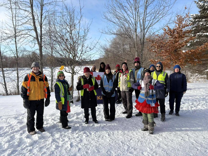 A group of parkrun volunteers taking pictures holding Canadian flags in snow at a parkrun event in Canada.