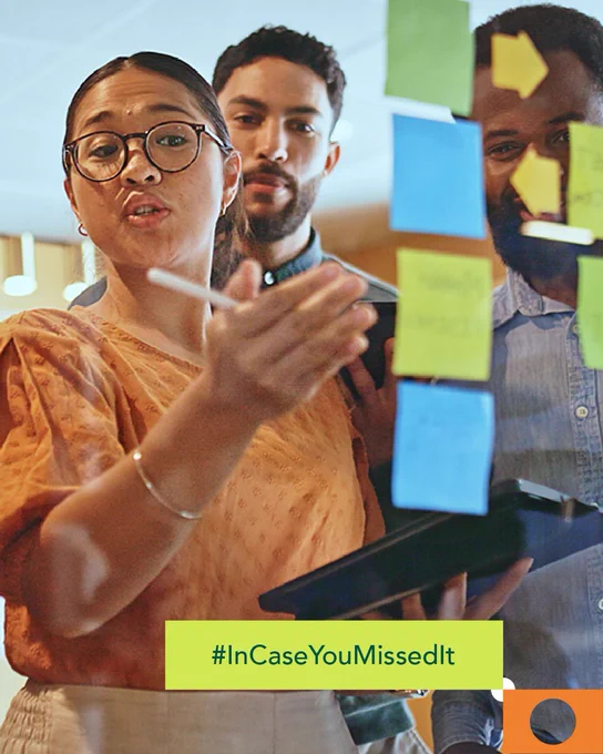 Group of professionals discussing ideas while reviewing sticky notes on a glass board 