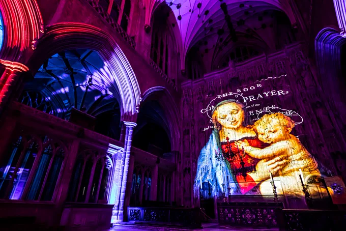 Projection of Madonna and Child illuminates a cathedral's arched interior in vibrant hues of purple and blue, evoking a serene, mystical ambience.