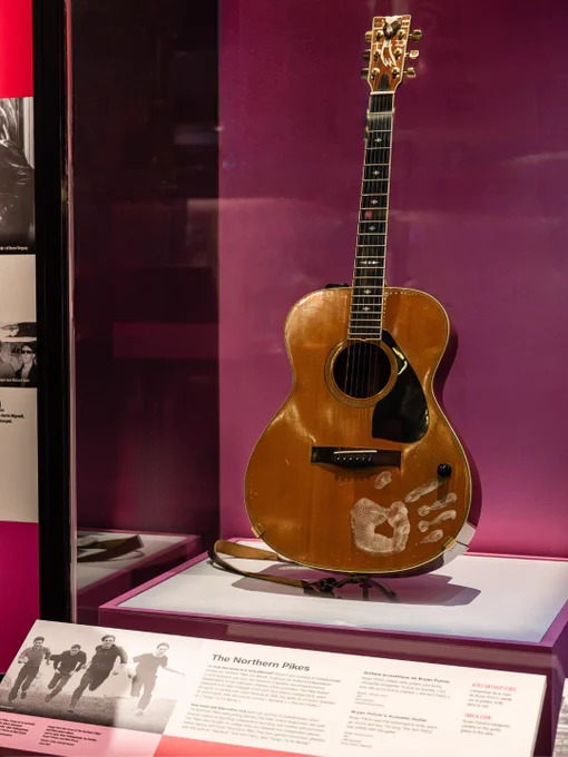 Une guitare acoustique avec une empreinte de main, exposée dans une exposition de musée dédiée aux Northern Pikes.