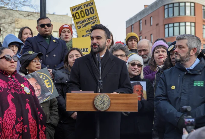 Mayor Zohran Mamdani speaks at a podium, surrounded by street safety advocates and government officials.