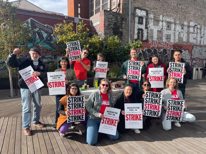 A dozen people holding strike signs. One displays a fist of solidarity.
