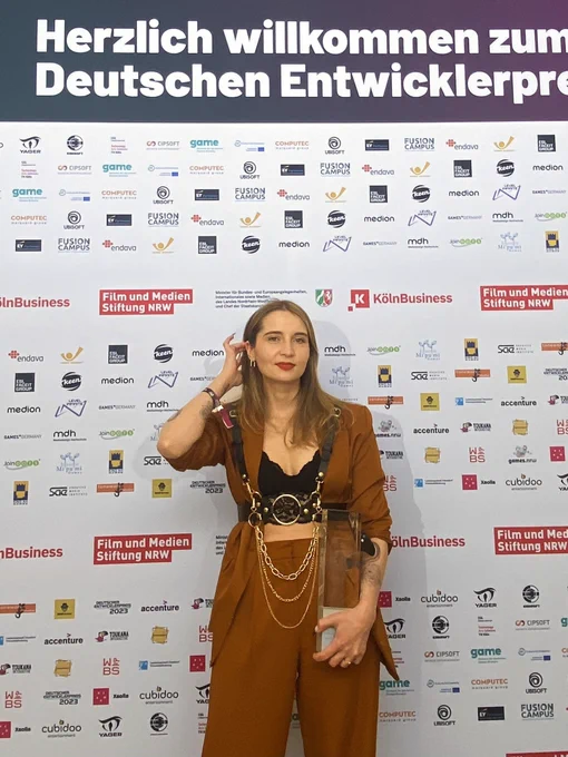 Woman in orange suit posing with award in front of foto wall.