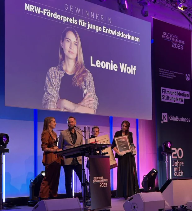 Woman standing on stage accepting an award from two men and another woman at Deustcher Entwicklerpreis.