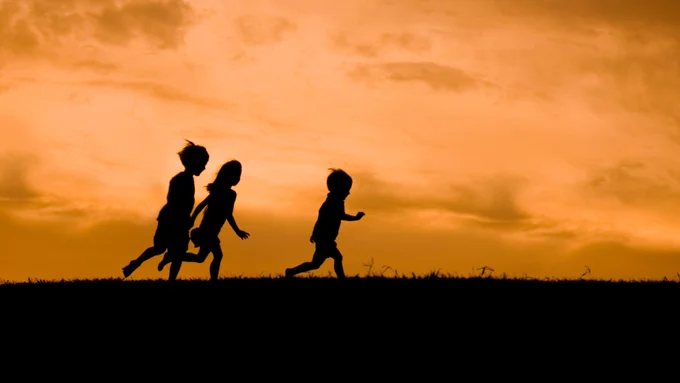 Photo of silhouettes of three children, running.