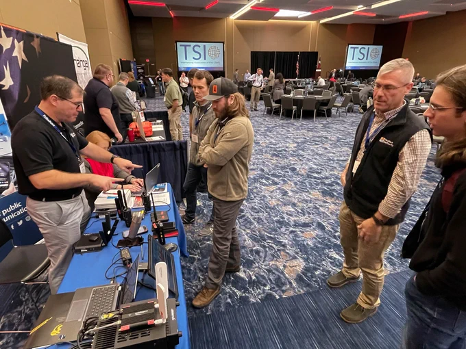 A FirstNet Authority representative behind a booth demonstrates tech to an attendee at the IAFC TSI conference