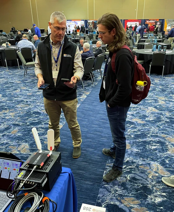 A FirstNet Authority representative behind a booth demonstrates tech to an attendee at the IAFC TSI conference