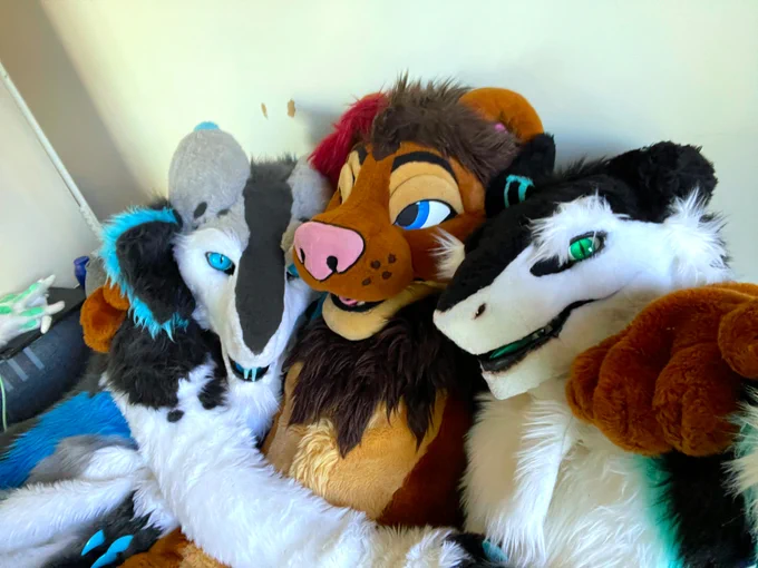 Three fursuiters cuddling and looking at the camera.