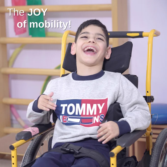 A male child in a yellow wheelchair with a big smile on his face.