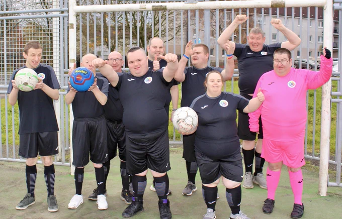 Group picture of everyone standing in front of a goal smiling and waving in the new strips. 