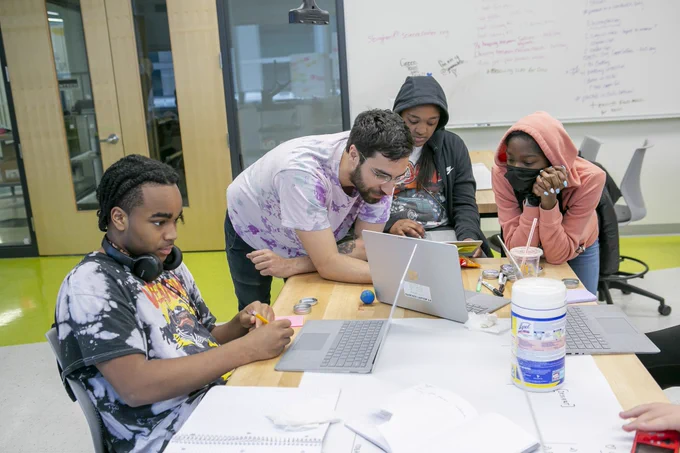 Students gather around computers in a classroom setting. 