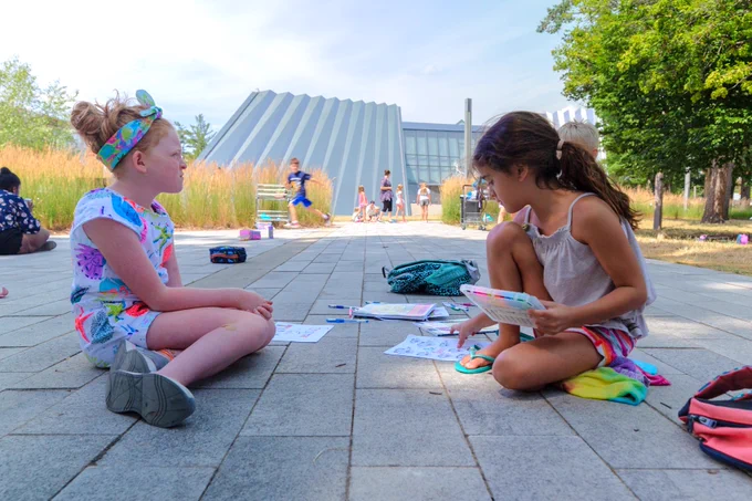 Two young girls, sitting on the ground and coloring, outside of the MSU Broad Art Museum
