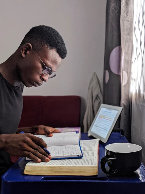 Person studying at a desk with a notebook, textbook, and tablet. 