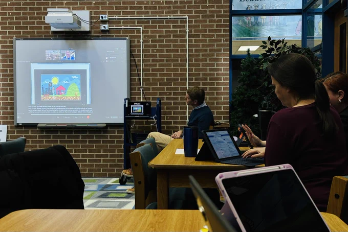 Presentation white board on a brick wall with teachers looking on, learning to use iPads.