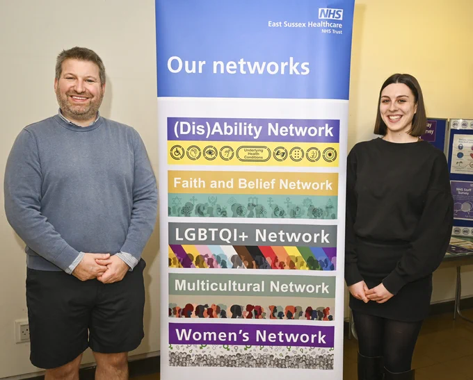 Photo of two East Sussex Helathcare NHS Trust (dis)Ability network members standing beside a banner depicting the names of all the networks at ESHT 