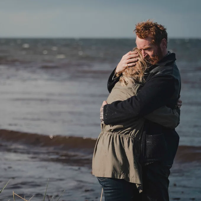 Still from Mayflies. Tony Curran and Ashley Jensen hug on a beach.