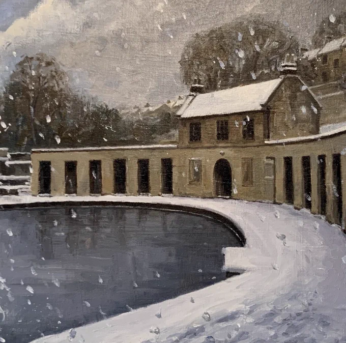 A winter view of a crescent shaped Georgian building behind an outdoor swimming pool. There is snow falling and settled on the ground. There are trees in the background.