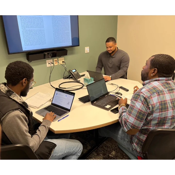 Three individuals working on laptops at a presentation table. 