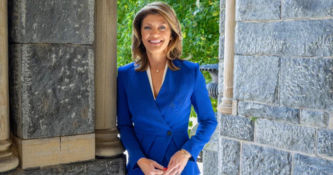 A woman smiling while leaning on a pillar of a stone building.