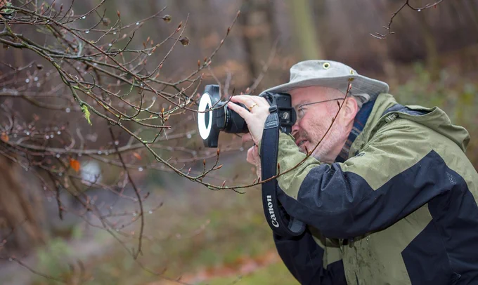 A photograph of a man with a camera taking photos in woodland.