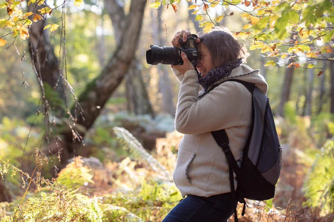 A photo of a lady taking photographs in woodland.