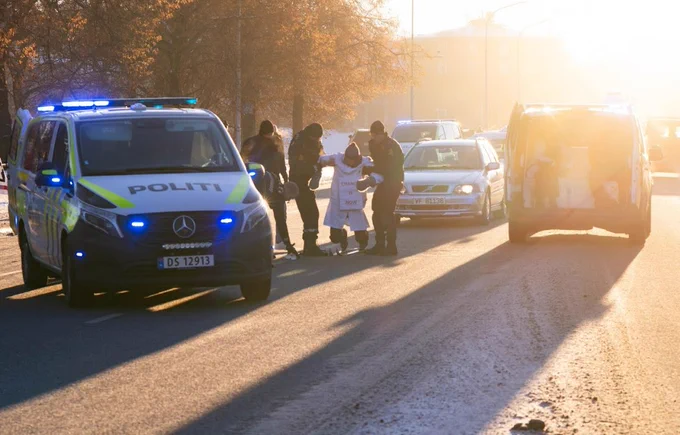 Strong sunshine as a scientist in a lab coat wearing skis gets arrested by police in Trondheim today. Photo: Ivain Martinossi.