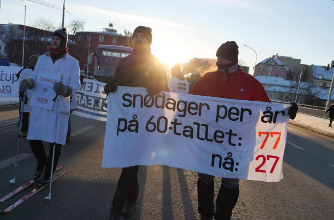 Protesters marching in streets in Trondheim. Two carry a banner "snow days per year in the 60s: 77. Now: 27." A scientist in lab coat is walking on skis, carrying a sign saying "Change is NOW". Photo: Denis Zimarev.