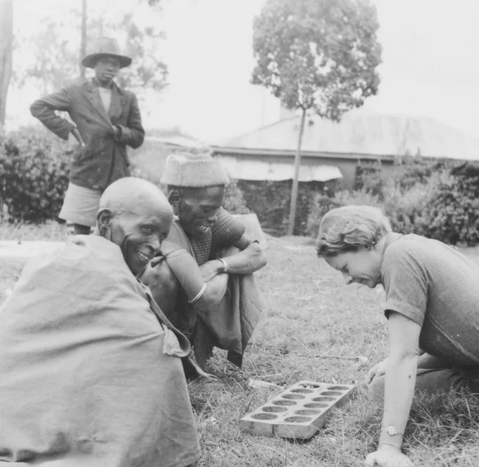 Elspeth Huxley plays a mancala game with two Kikuyu men at Njoro, Kenya in the 1930s 