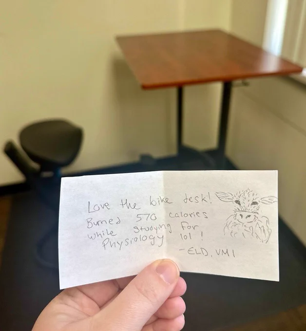 Scrap of paper with a note and a drawing of a buff cow in front of the library's bike desk. Note reads: "Love the bike desk! Burned 570 calories while studying for Physiology!" 