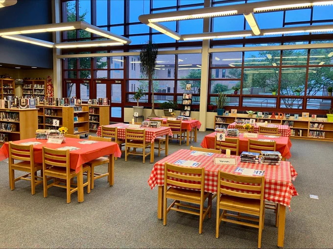 Tables in a library are covered in plastic red and white checkered table cloths with book displays.