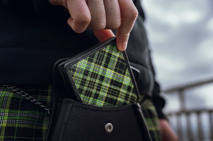 A hand reaching down, holding an Xbox Tartan wallet from the Xbox x Gordon Nicolson Kiltmakers collection, and placing it in a sporran (the pouch in front of a kilt).