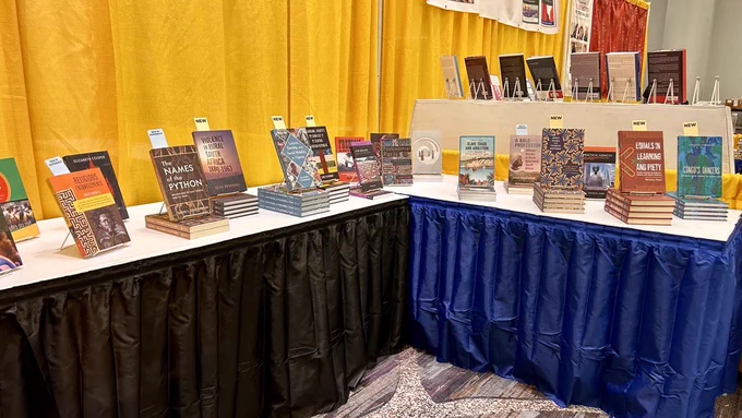 A photo of the UW Press booth at ASA (African Studies Association) conference 2023. In the background, there's a yellow curtain. In the foreground, there's a table with dark blue skirts with lots of recent books on display.