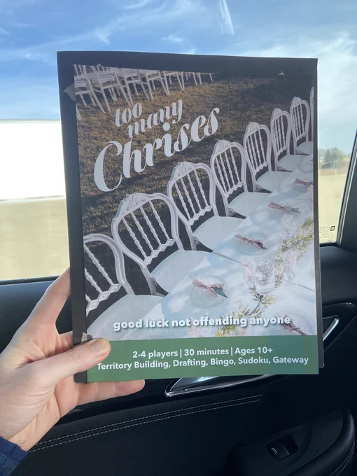 A hand holding a letter sized flyer in a car that reads “too many Chrises” in script over an image of an outdoor wedding reception.