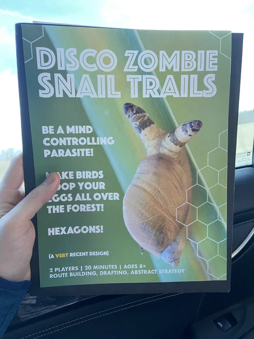 A hand in a car holding a letter sized flyer that reads “Disco Zombie Snail Trails” over a macro photo of a snail parasitized by Leucochloridium in its eye stalks