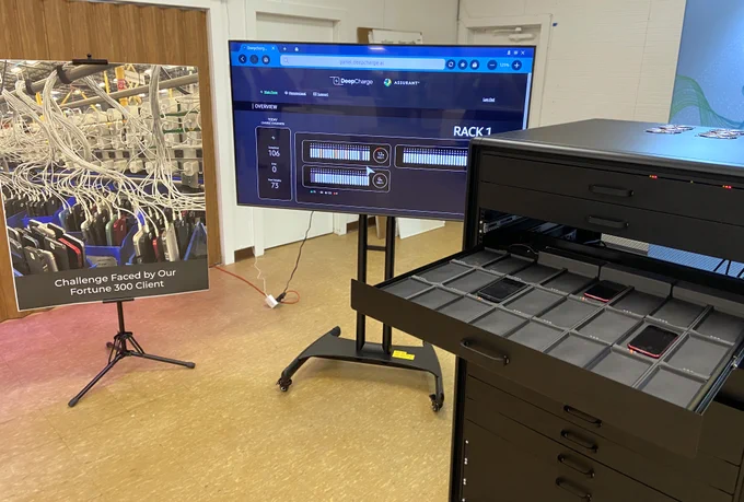 DeepCharge Rack has a drawer pulled out with multiple phones charging at once. A large TV screen next to it shows the power level of each phone.