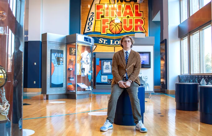 Conor Kerr sits in front of the exhibits at the Carolina Basketball Museum. Behind him is the NCAA "Final Four" logo from the tournament in St. Louis in 2005.