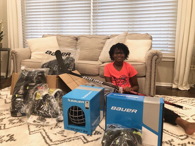 Bauer grant recipient Victoria Blake sits on the floor in a pink shirt posing for a photograph in front of brand new Bauer equipment.