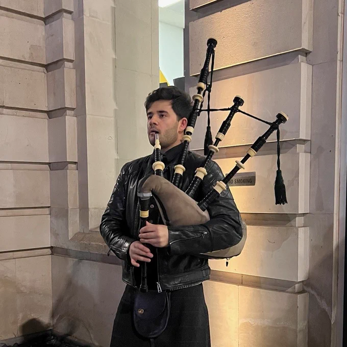 A photo of Séamus Ó Baoighill stood outside playing a bagpipe 