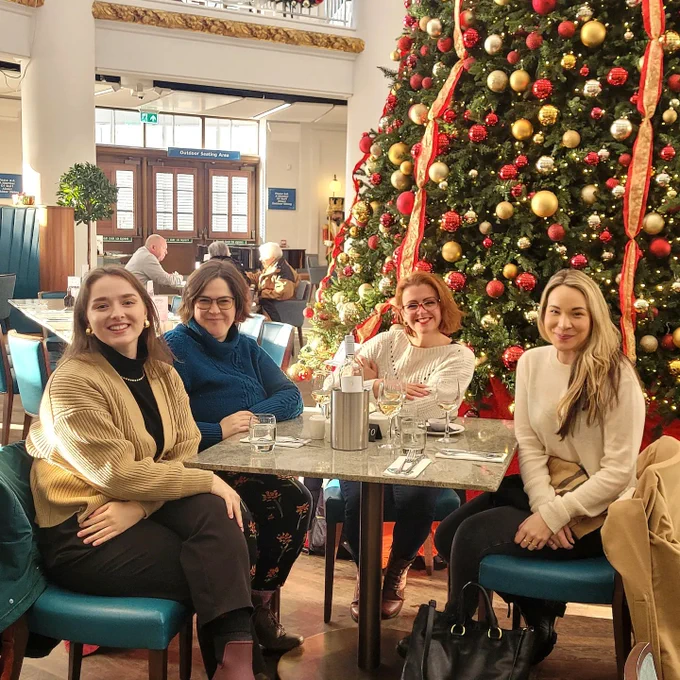 This is a photo of Ruth, Katie, Vicky and Claire. They are sat at a square dining table in a restaurant in front of a very large, decorated Christmas tree.