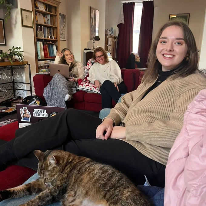 This is a photo of Claire, Vicky and Ruth. They are sat on sofas in Katie's home, smiling at the camera. Ruth is in the foreground and Claire and Vicky are further back.