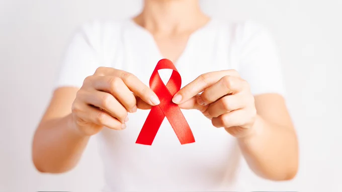 Nahaufnahme Frauenhand, die rote HIV Schleife hält 