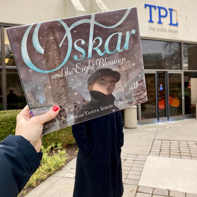 Bookface cover of 'Oskar and the Eight Blessings' by Richard and Tanya Simon in front of the Troy Public Library