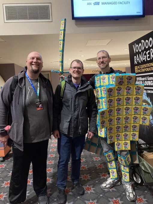 Shawn, dressed in a ridiculous suit, made out of sweet deals boxes, stands with a Kickstarter backer