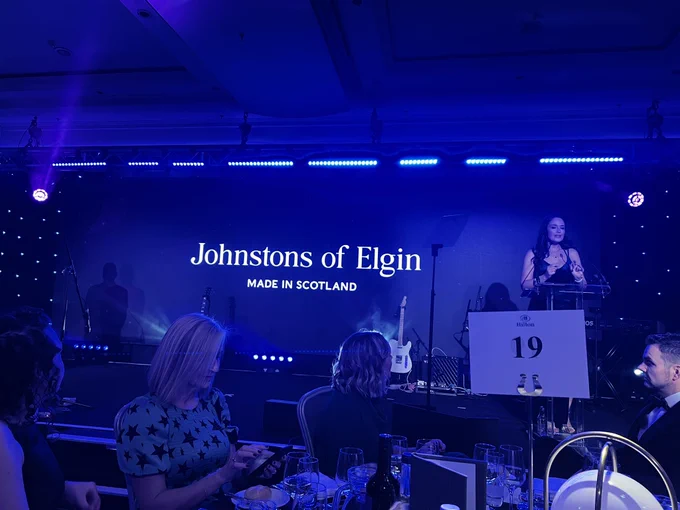The stage for the awards with the presenter to the right at a lectern and a the sponsors name ‘Johnston’s  of Elgin’ above the stage