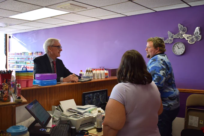 Gov. Evers stands at counter, talking with owners of a crafts and arts store in Antigo.